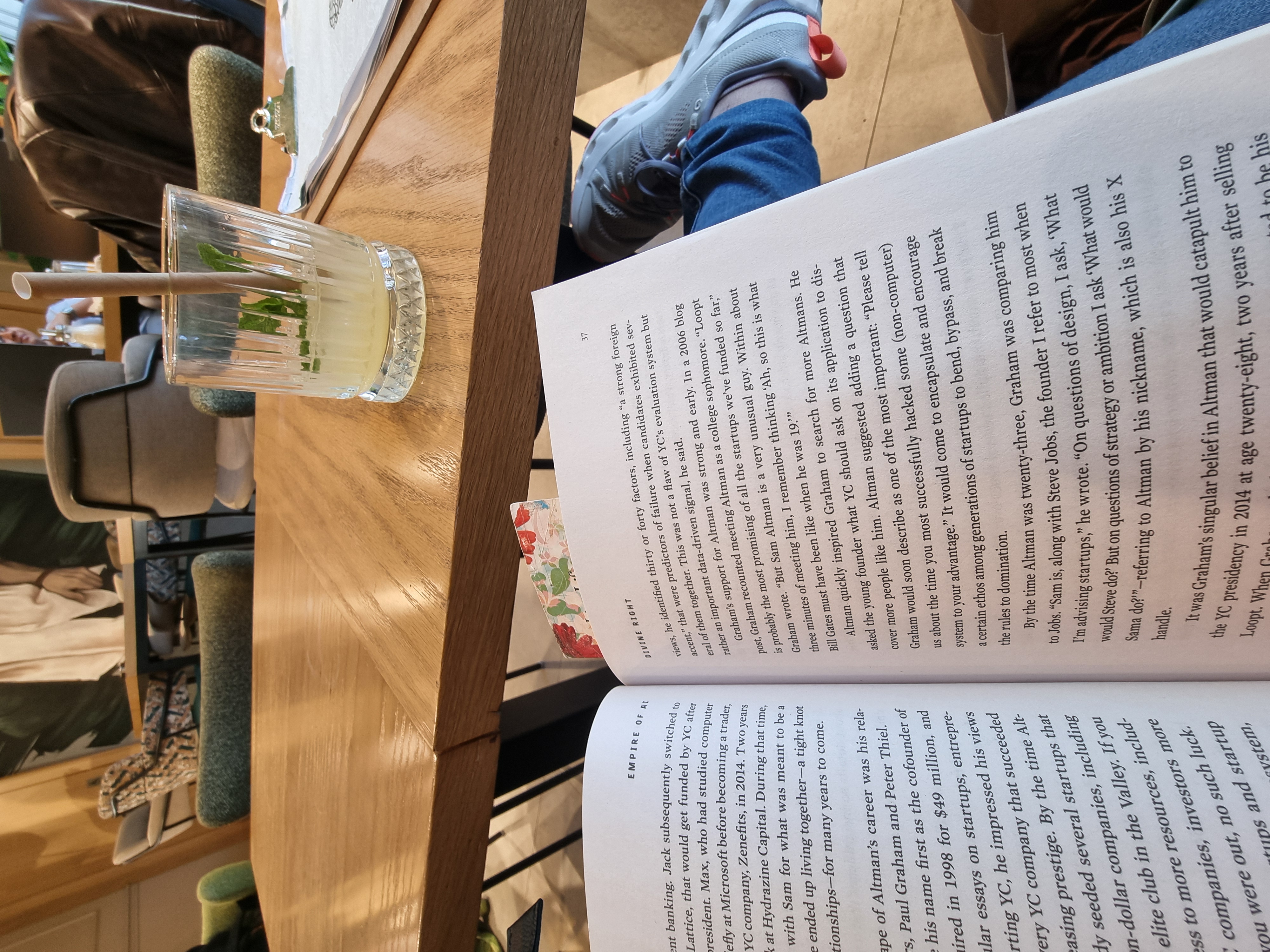 An open copy of Empire of AI beside a glass of lemonade at a caf&eacute; table.